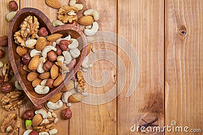 Natural nutritious mix of different nuts in a wooden plate of heart symbol shape on brown wooden table at the left side. Mixture o Stock Photo