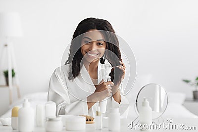 Natural products and cosmetics for hair. Happy african american woman applying essential oil spray on curly hair Stock Photo