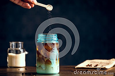 Natural Raw Sugar Pouring Into Iced Organic Coffee Served In Blue Jar Stock Photo