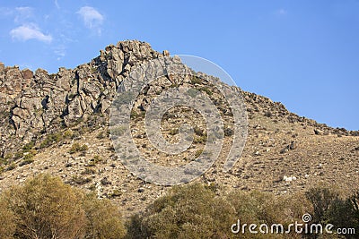 Natural rocky hill in daylight, plants and clear blue sky in the background Stock Photo