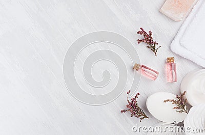 Natural spa cosmetics with pink rose oil, salt, soap and lavender flowers on white wood background, top view, border. Stock Photo