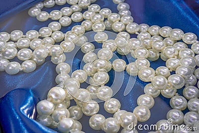 Natural White Pearls in the water on a blue silk texture close-up. Pendants on the neck. Stock Photo