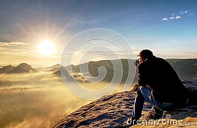 Nature photographer create art on view point in mountains. Man looking into viewfinder of his big camera, taking photo of borning Stock Photo