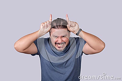 A naughty man with a devilish smile making horn signs with his fingers on his head. A playfully fiendish guy Stock Photo