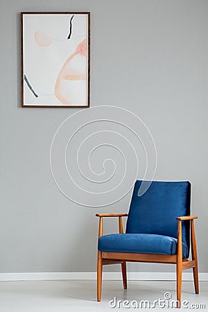 Navy blue wooden armchair in simple grey living room interior with poster on the wall Stock Photo