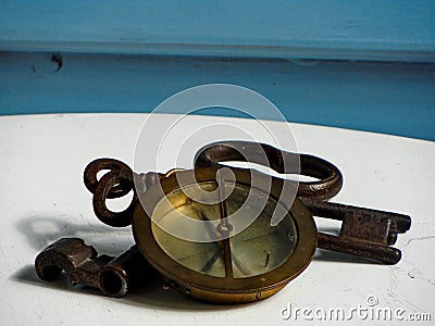 Navy compass and three solid iron, rusted keys on white and blue background. Stock Photo