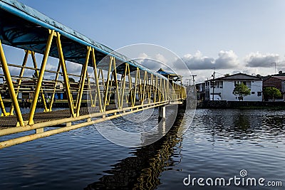 Iron pedestrian walkway over a river in yellow and blue colors. Reflection in water Editorial Stock Photo