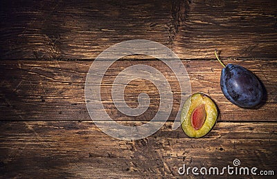 Ðžne single plum and a half of plum with stone over dark wooden board. Fruit background. Text space. Top view. Stock Photo