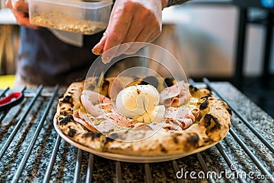 Neapolitan pizza style: close-up chef hand seasoning crushed pistachio over mortadella and burrata pizza on the pizza cooling rack Stock Photo