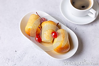 Neapolitan Rum baba or baba au rum on a white plate with a cocktail cherry and a cup of coffee. Small yeast cakes soaked in rum Stock Photo