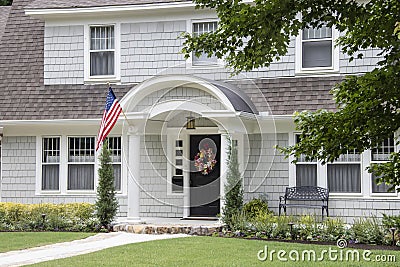 Neat and pretty shingled retro house with arched entryway and beautiful landscaping with colorful summer wreath on front door and Stock Photo