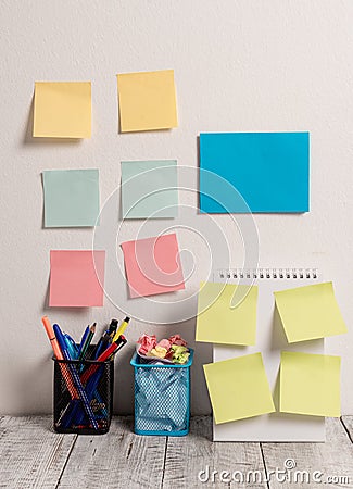 Neat Workplace with Blue Card and 10 Empty Colored Stick Pad Notes Put on Both White Wall and Open Spiral Notebook with Stock Photo