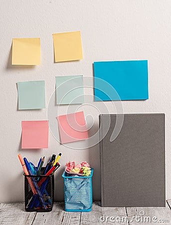 Neat Workplace with 6 Empty Colored Stick Pad Notes and Blue Card Put on White Wall and 2 Full Pencil Pots next to Grey Stock Photo