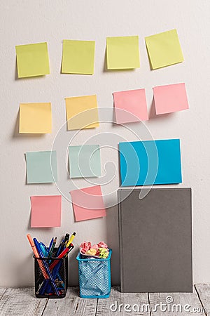 Neat Workplace with 12 Empty Colored Stick Pad Notes and Blue Card Put on White Wall and 2 Full Pencil Pots next to Grey Stock Photo