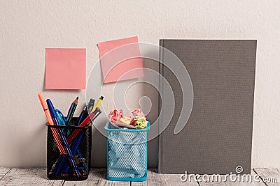 Neat Workplace with Empty Colored Stick Pad Notes Put on White Wall and Two Full Pencil Pots and Grey Hardcover Notebook Stock Photo