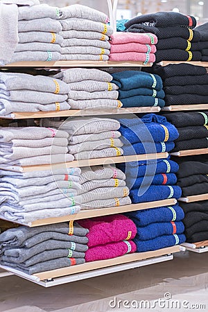 Neatly folded clothes. Rack of clothes with warm. Wooden cabinet with a stack of sweaters. Coloured clothing. Neat stacks of Stock Photo