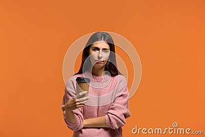 Need to cheer up. Tired sleepy beautiful woman in pink sweater with a tortured look has sad expression, carries disposable cup of Stock Photo