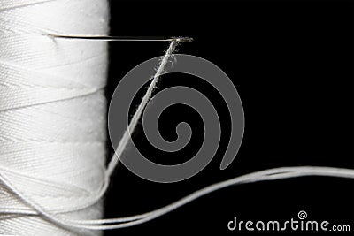 Needle stuck in white coil thread on black background macro Stock Photo