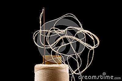 Needle and white cotton, tangled yarn on roll for sewing. Thread used in fabric and textile industry. Black background Stock Photo