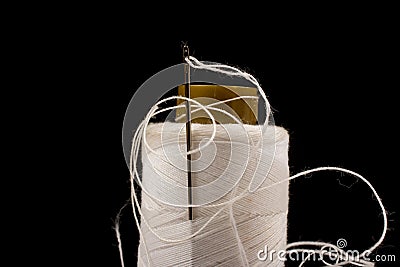 Needle and white cotton, tangled yarn on roll for sewing. Thread used in fabric and textile industry. Black background Stock Photo