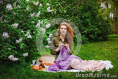 Needlework in the garden. Young woman crocheting sitting on the grass in the park. Picnic and leisure, knitting in nature Stock Photo