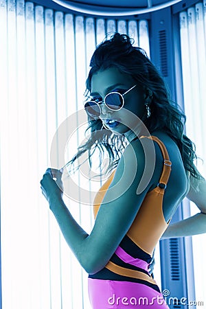 Neon light and sexy hipster girl. Young beautiful athletic woman model in a stylish color swimsuit in vintage sunglasses with Stock Photo