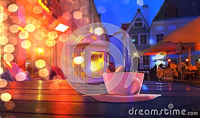 Neon night city blurred light street restaurant yellow coffee cup lantern on wooden table medieval house in Tallinn Old Town Eston Stock Photo