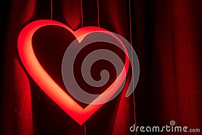 Neon red heart sign glowing against a dark curtain, symbolizing love Stock Photo