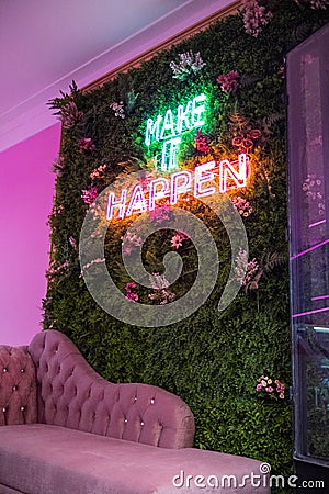 Neon sign on wall of green leaves above pink couch Stock Photo