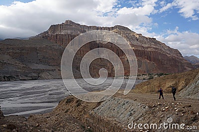 Tourists with trekking chopsticks walk along the Kali Gandaki River against the backdrop of the Chhusang cliffs. Stock Photo