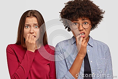 Nervous anxious two women bite finger nails with anxiety, worry about something, stand shoulder to shoulder, pose Stock Photo
