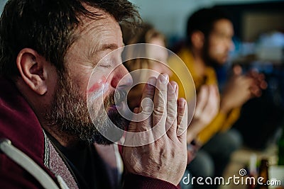 Nervous football fans friends watching match on TV at home and praying. Stock Photo