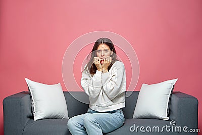 Nervous scared anxious woman biting nails, feeling fear, thinking about problem, sitting on sofa. Domestic violence Stock Photo