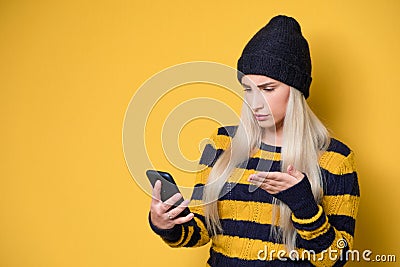 Nervous woman holding mobile phone, model wearing woolen cap and sweater, isolated on yellow background. No Wi-fi concept. Bad Stock Photo