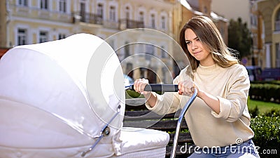 Nervous young woman trying to calm down crying baby in stroller, baby colic Stock Photo