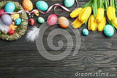 Nest with Ñolorful easter eggs, flowers and feathers on wooden background. Festive tradition. Space for text Stock Photo