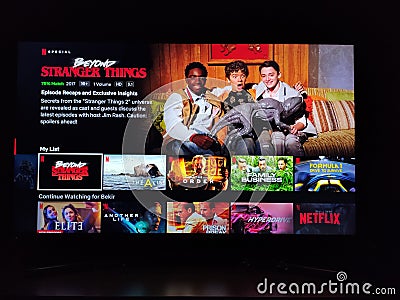 Netflix app on tv screen playing and the `Beyond Stranger Things` series logo behind. Editorial Stock Photo