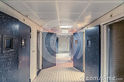 NETHERLANDS-FEBRUARY 24: An empty corridor of a prison with tiles on the floor and open steel cell doors on which texts are Stock Photo