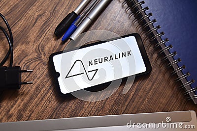 The Neuralink logo is seen on a smartphone screen on a table with objects in the background Editorial Stock Photo