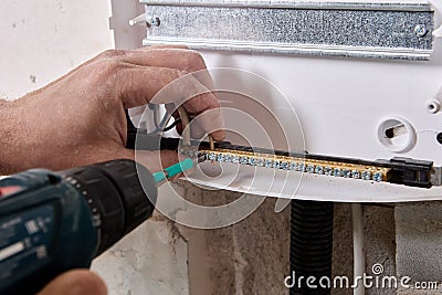 An electrician fixes ends of wires in brass distribution bar using an electric screwdriver. Stock Photo