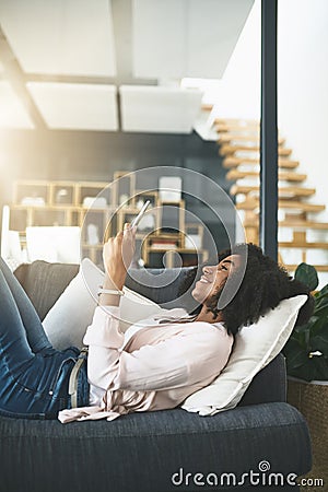 Never alone with technology keeping her connected. an attractive young woman relaxing at home. Stock Photo
