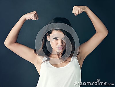 Never apologize for being a powerful woman. Studio shot of a beautiful young woman flexing her muscles against a dark Stock Photo