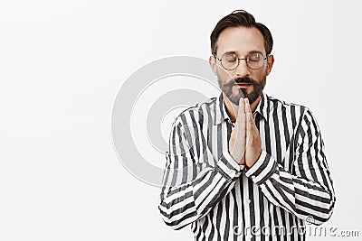 Never forgets to thank god for success. Calm and relaxed good-looking believer in glasses and striped shirt, holding Stock Photo