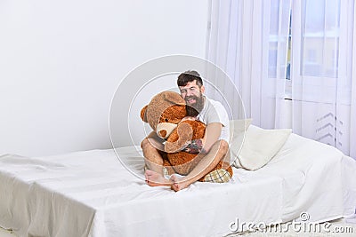 Never grow up concept. Guy on happy face hugs giant teddy bear. Macho with beard and mustache cuddling with plush toy Stock Photo