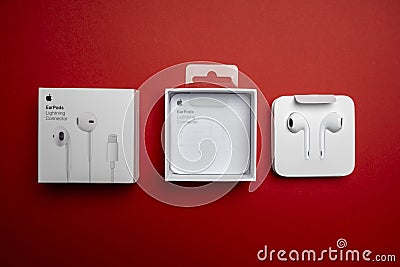 New Apple Earpods, Airpods white earphones for listening to music and podcasts in an open box. Isolated red background. Editorial Stock Photo