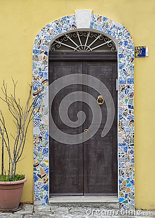 New dark brown wooden door with a stone arch decorated with broken patterned tiles in Italy Editorial Stock Photo