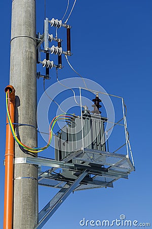 New distribution transformer on concrete power pole with external electric separator against the blue sky. Stock Photo