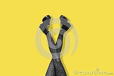 New gray female boots with bright yellow laces on long slender crossed woman legs in gray tights isolated on yellow background. Stock Photo