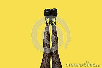 New gray female boots with bright yellow laces on straight, long slender woman legs in gray tiger print tights isolated on yellow Stock Photo