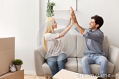 New Home. Happy Couple Giving High Five Sitting On Couch Stock Photo